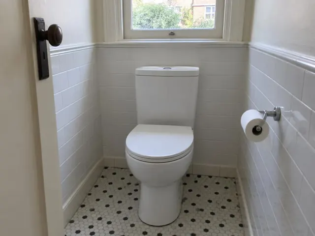 Clean white toilet in a small tiled bathroom with a window and patterned floor in Willoughby